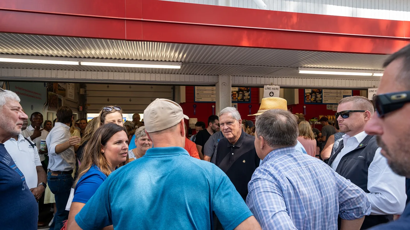 Fairgoers crowded shoulder to shoulder at a red-roofed food stand