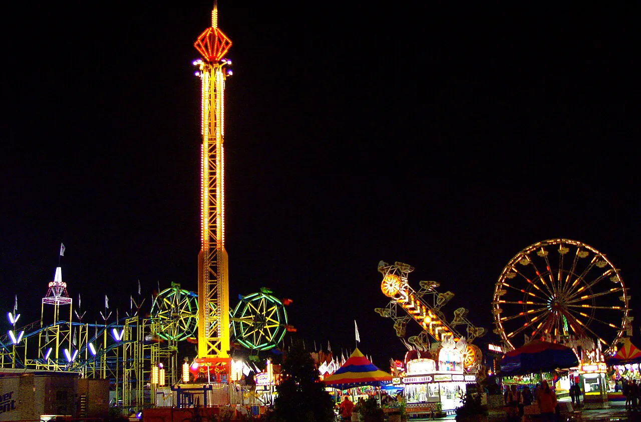 The Mighty Midway lit up after dark, with the drop tower and Ferris wheel above the game stalls